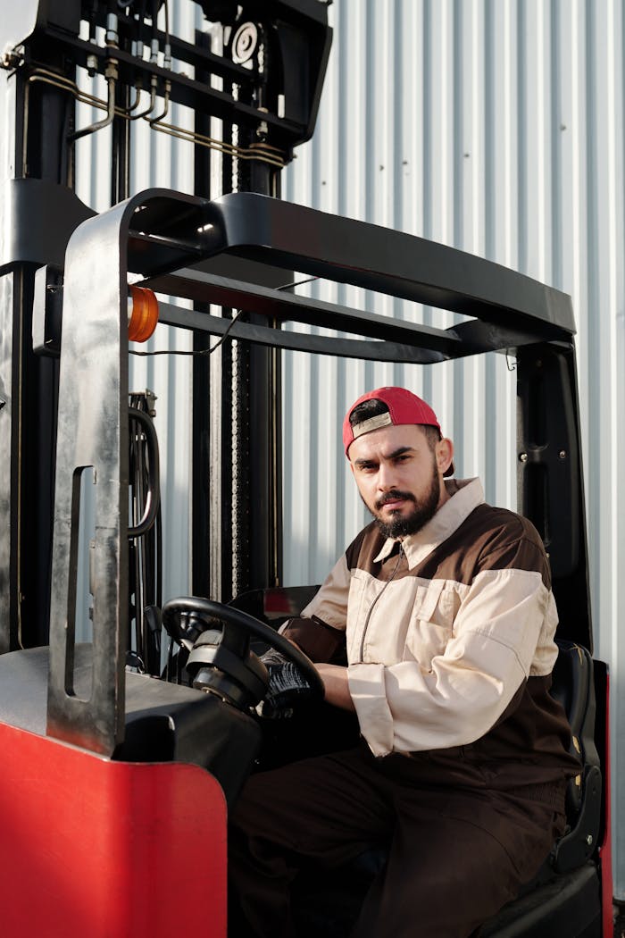 Portrait of a forklift operator inside a warehouse, wearing a uniform and cap.