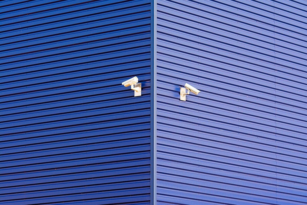 Minimalist image of a blue wall with two CCTV cameras emphasizing security and technology.